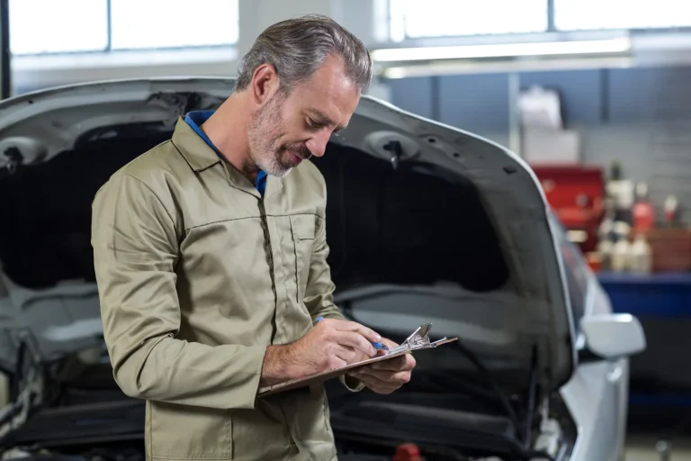 Mechanic ticking a checklist on a clipboard beside an open car bonnet