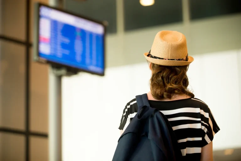 Traveller in a straw hat glancing up at an airport information screen