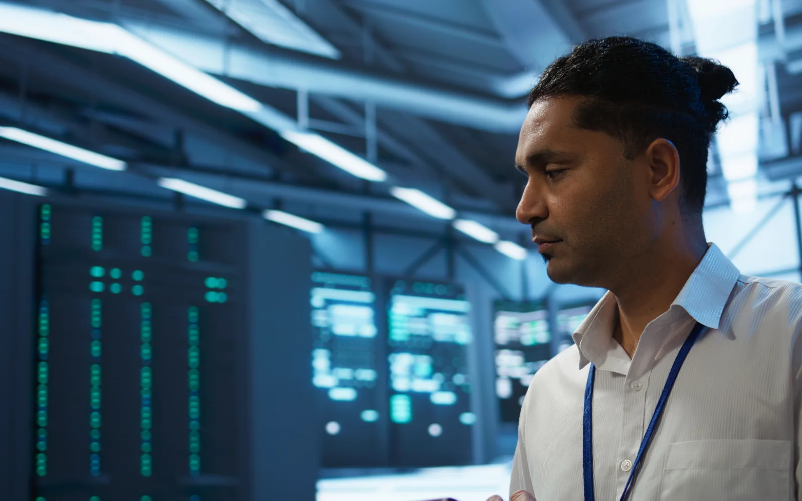 Engineer wearing a lanyard checking equipment inside a large data centre